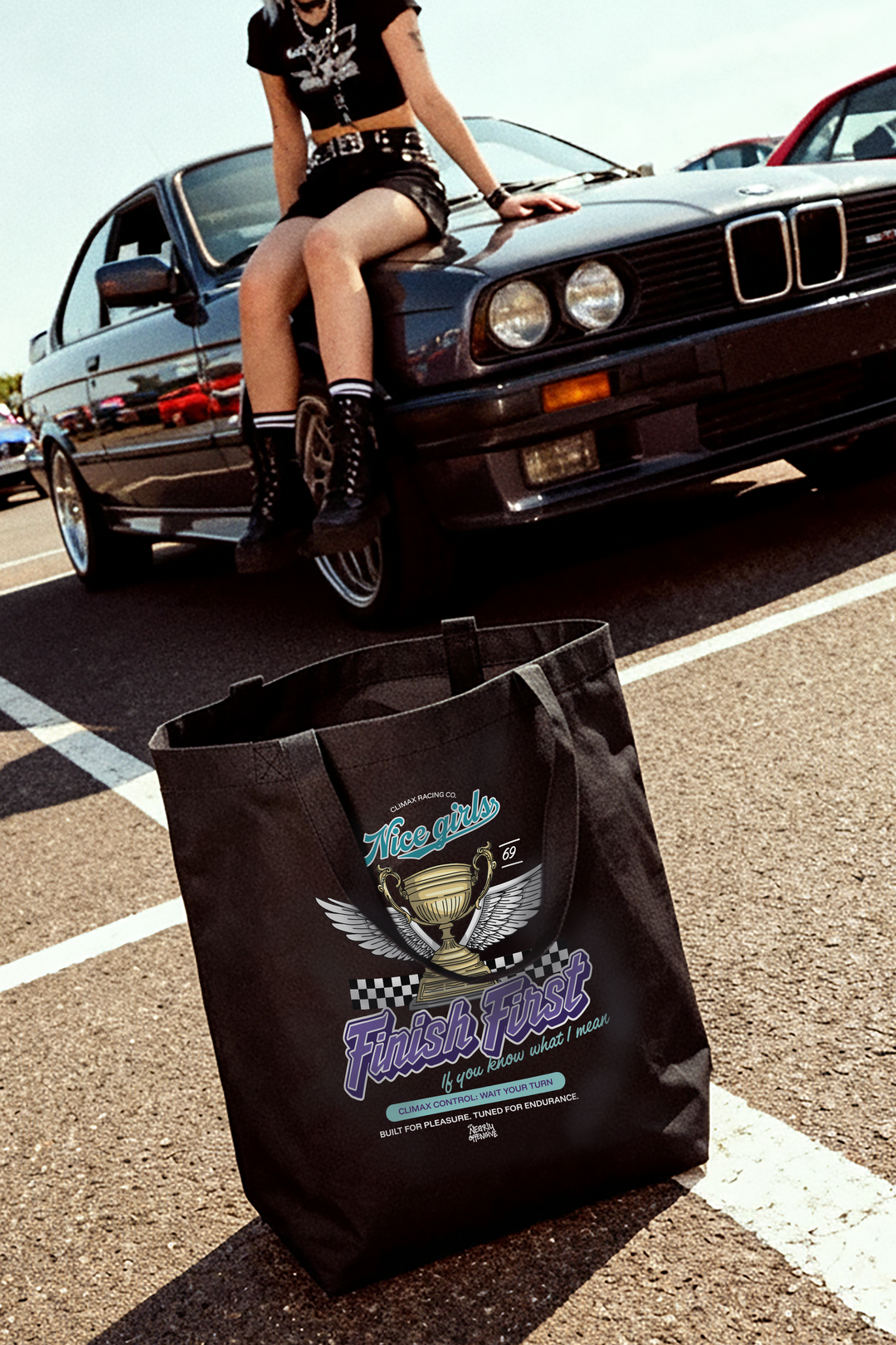 Person sitting on a car with a black tote bag featuring a logo and text on a road.