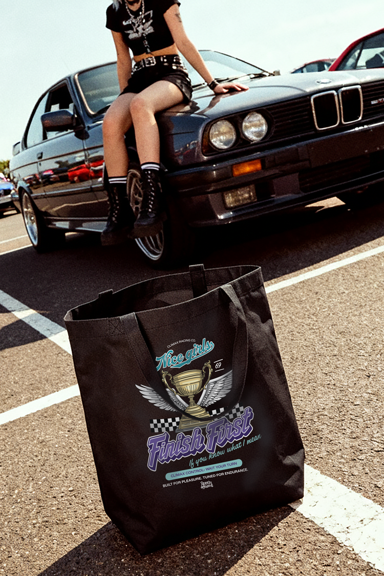 Person sitting on a car with a black tote bag featuring a logo and text on a road.